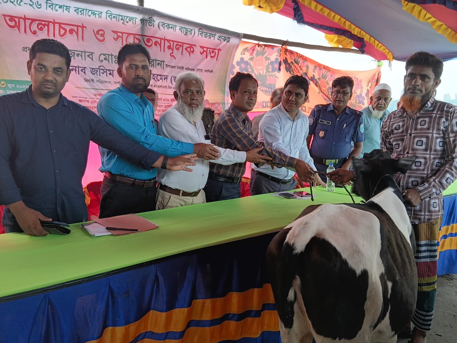 Cow distribution handover to beneficiary under tent.